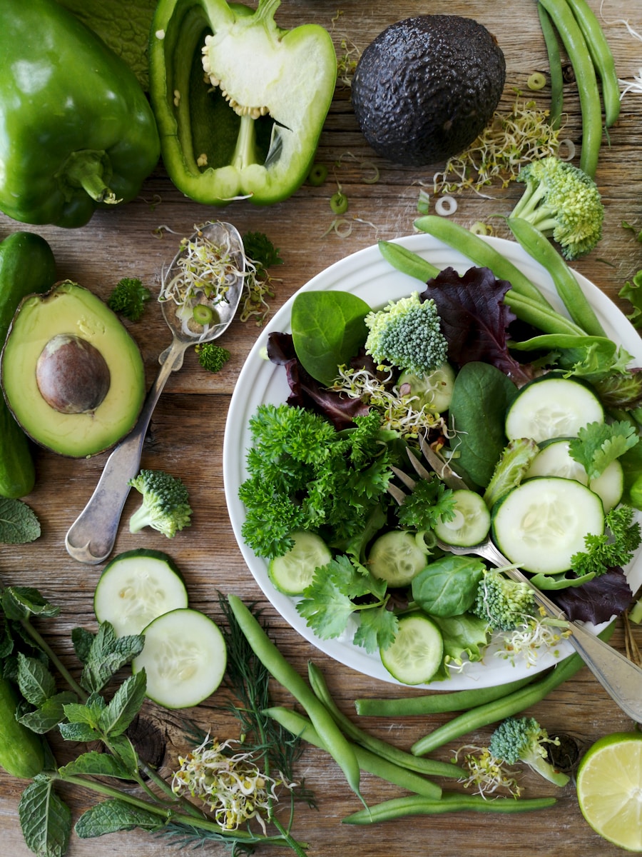 sliced broccoli and cucumber on plate with gray stainless steel fork near green bell pepper, snowpea, and avocado fruit