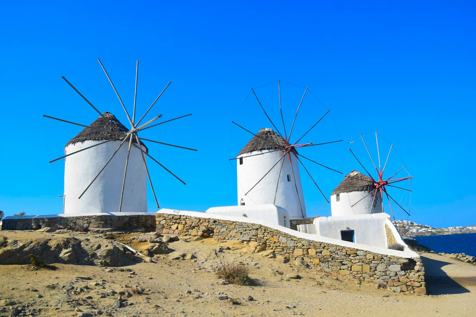 a group of windmills on a hill with Mykonos in the background
